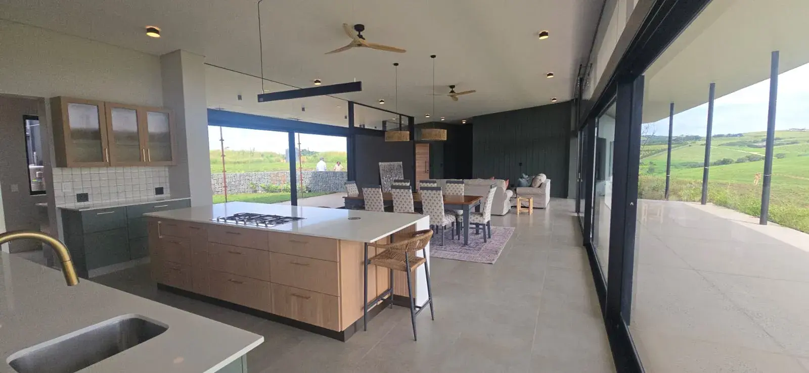 JehCon open-plan kitchen renovation with an oak island, gas hob, sage green cabinetry and sliding doors opening onto countryside views